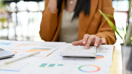Female accountant or financial office manager working at her office desk, using calculator and...