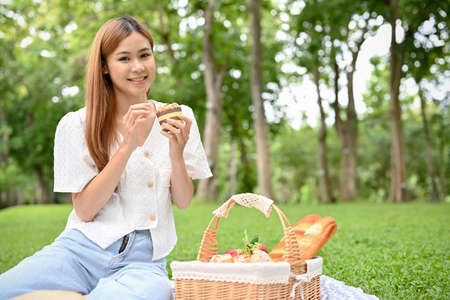 Lovely and happy young Asian female picnics in the beautiful green garden in sunny summer day. Outdoor activity conceptの写真素材