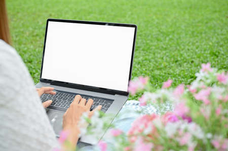 A young Asian female or college student sits under the tree in the park using her laptop computer....