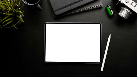 Hipster photographer office workspace with digital tablet touchpad white screen mockup, film camera, and accessories on black background. top view, flat layの写真素材