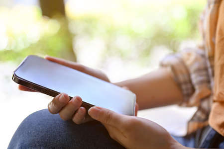 close-up image, A female freelancer or college student sits in the park and uses her modern...