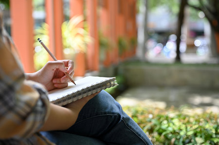 A hipster female freelancer noting her creative ideas or planning her project in a notebook while...