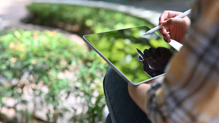 A female college student noting her project ideas on her tablet touchpad while relaxing sits in the campus's park. close-up imageの写真素材
