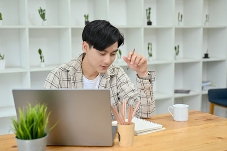 Concentrated young Asian male college student or freelancer working and planning his project in his working room.の写真素材