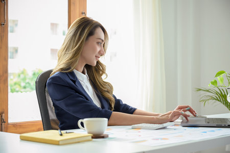 Cheerful and beautiful young Asian businesswoman or female banker using laptop computer, working at her office desk.の写真素材
