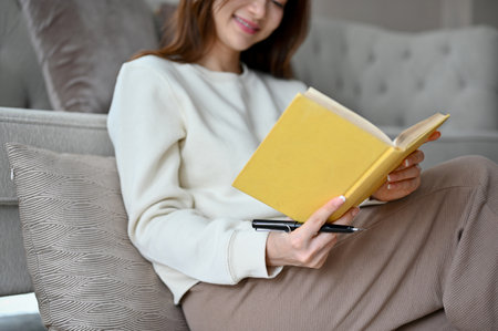 A beautiful young Asian female chilling in her living room, reading a book or playing a word scramble game on her book. cropped imageの写真素材