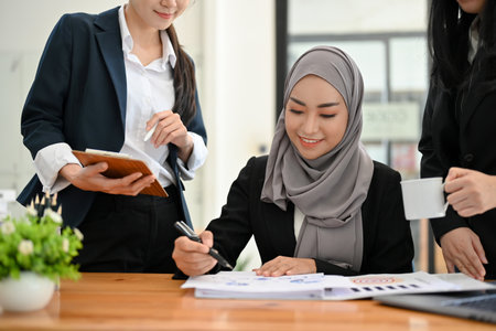 A beautiful young Asian Muslim businesswoman or female financial analyst having a financial meeting with her team in the office.の写真素材