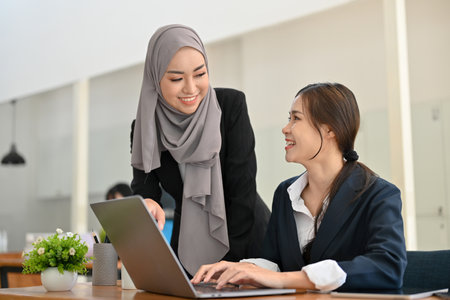 Professional and attractive young Asian Muslim businesswoman talking and discussing the marketing plan with her female colleague in the office.の写真素材