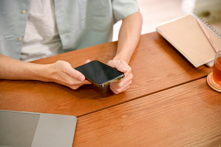 A man sitting at his office desk and using his smartphone to contact with his coworkers. cropped...