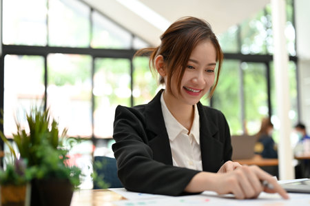 Pretty young Asian businesswoman sits in the office co-working space working on her financial report paperwork.の写真素材