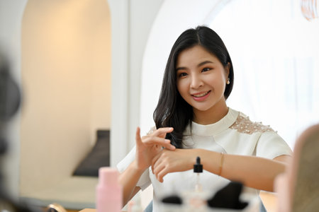 Charming asian female make-up artist or freelance beauty blogger broadcasting live streaming to review her serum treatment to her online followers.の写真素材