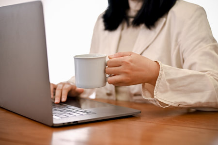 An Asian businesswoman or female manager sipping her morning coffee while working on laptop computer. cropped shotの写真素材