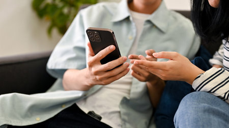 Lovely teen couple looking something on a smartphone while relaxing in their living room together....