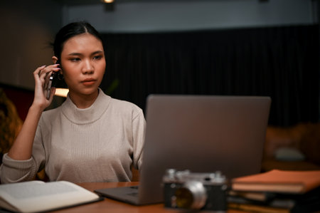 Confident and professional Asian businesswoman or female boss talking on the phone with her business partner while working in the office at night.の写真素材