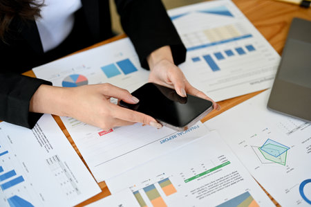 A businesswoman using her mobile phone while working on her business report assignment in the...
