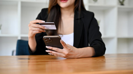 A beautiful Asian female or businesswoman sits at her office desk holding a credit card and a...