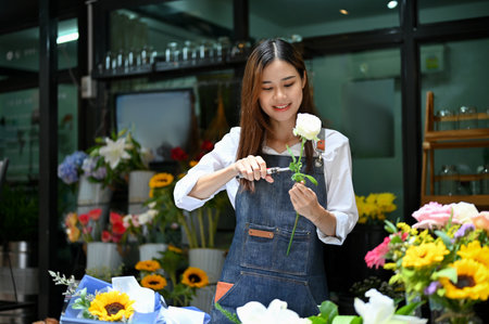 Charming and cheerful young Asian female florist or flower shop owner making a beautiful roses bouquet for her customer.の写真素材