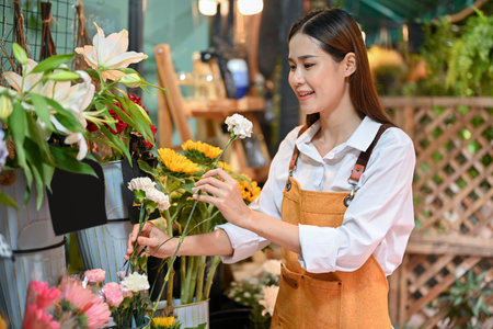 Attractive young Asian female florist or flower store owner arranging flowers in a vase in her shop. Small business owner conceptの写真素材