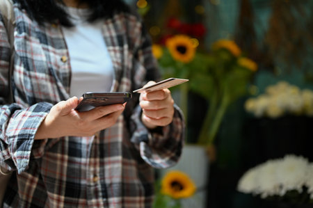 cropped image, An Asian female customer holding a smartphone and a credit card, paying her stuff...