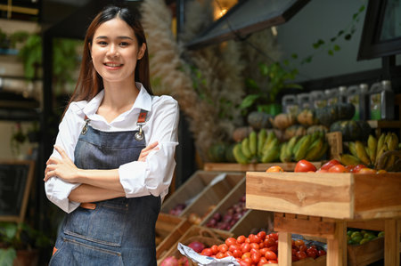 Portrait, Attractive and successful young Asian female local grocery shop owner or worker in apron arms crossed, standing in front of her shop. Small business conceptの写真素材