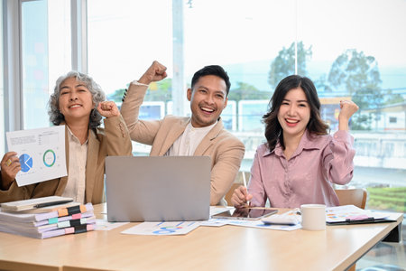 Happy and cheerful Asian businesspeople or a financial analysts team showing triumphs, smiling, looking at the camera, celebrating their success together.の写真素材