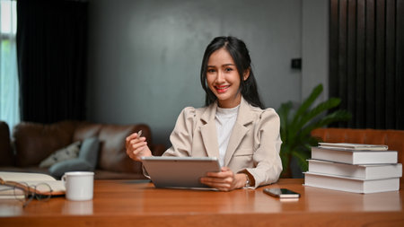 Charming beautiful young Asian businesswoman or female assistant using digital tablet at her desk,...