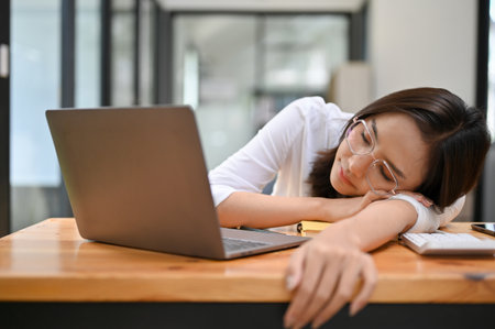 Tired millennial Asian businesswoman or female accountant falls asleep or takes a nap at her office desk. Overworked businesspeople conceptの写真素材