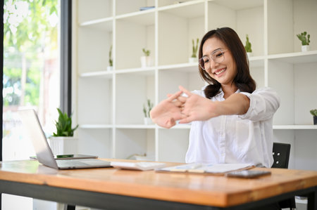 Positive and cheerful young Asian businesswoman or female office worker stretching her arms and hands at her office desk.の写真素材