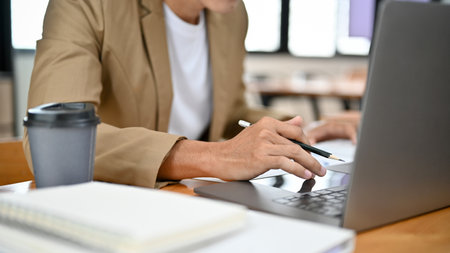Professional and smart Asian businessman or male boss working at his office desk, using laptop, typing on keyboard, doing his project on notebook computer. cropped and close-up imageの写真素材