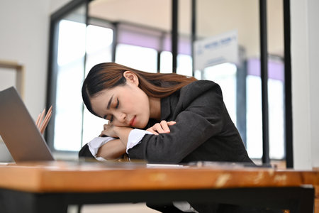 Tired, exhausted young Asian businesswoman or female office worker dropped head on hands, fall asleep at her desk, napping at her workplace.の写真素材