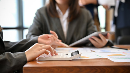 A female accountant using a calculator to calculate business investment income and tax during the meeting with her team. cropped imageの写真素材