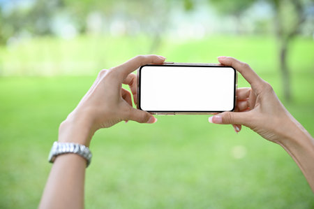 Close-up image, A female's hands holding a smartphone, using smartphone to taking a picture of the beautiful green view.の写真素材