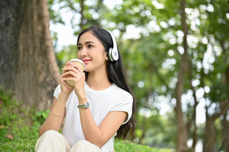 Attractive and charming young Asian female listening to music through her headphones and sipping...