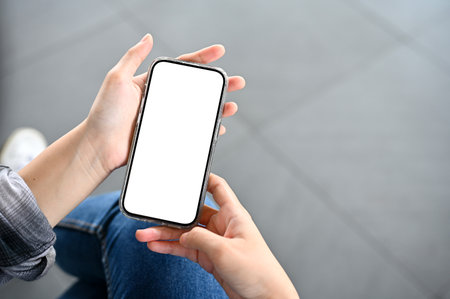 Top view, close-up image. A female hand holding a smartphone white screen mockup over blurred...