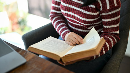 A smart young Asian female college student reading a book, researching information on textbook while sitting in the campus library. cropped imageの写真素材