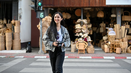 Young female tourist walking across the street and holding camera in her hand while traveling in...