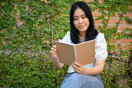 Beautiful young Asian woman enjoys reading book or novel in her beautiful garden or backyard. hobby and leisure conceptの写真素材