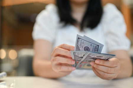 An Asian woman sitting at her desk, carrying a wad of 100 US dollar notes. financial concept....