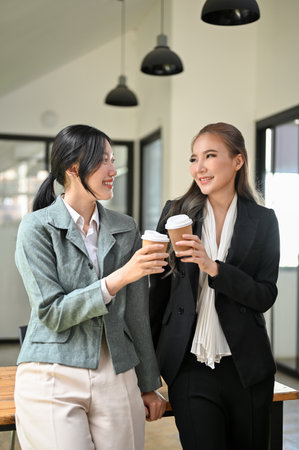 Portrait, Two beautiful and attractive millennial Asian businesswomen enjoy talking chatting during their coffee break in the office.の写真素材
