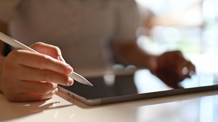 Asian female freelance graphic designer using her digital tablet and stylus pen to design her...