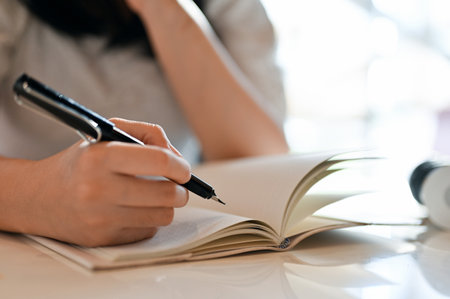 Young Asian female writing her diary or taking notes on her notebook, remote working at the coffee shop. cropped and close-up imageの写真素材