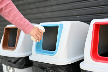A female's hand throwing an empty cup of coffee into the trash can. cropped and close-up image....