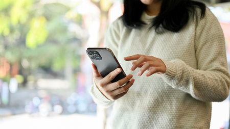 An Asian female in white sweater holding mobile phone, using her smartphone. chatting, reading...