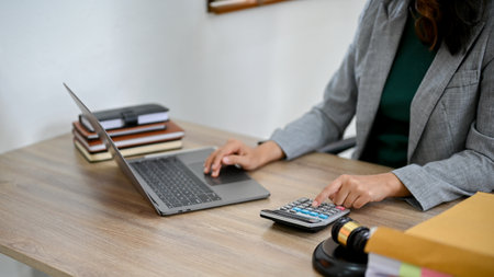 Professional Asian female lawyer working at her desk, using laptop computer and calculator. cropped...