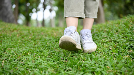 A hipster woman in casual clothes and white sneakers strolling in the green garden. cropped and close-up legs imageの写真素材
