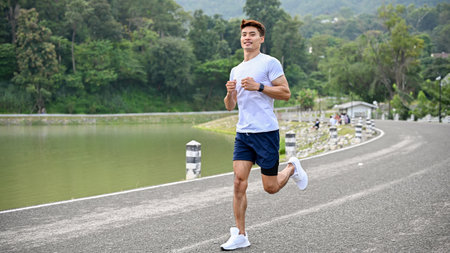Active and handsome Asian athletic man in sportswear and running shoes, running along the lake in...