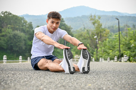 Active and handsome Asian athletic man in sportswear and running shoes stretching his legs on the...