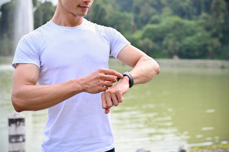 Handsome and athletic young Asian man in sportswear looking at his smartwatch, checking his heart...