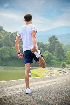 Fit and active young Asian athletic man in sportswear stretching his leg, warm-up before running. marathon, training, wellbeing. back viewの写真素材