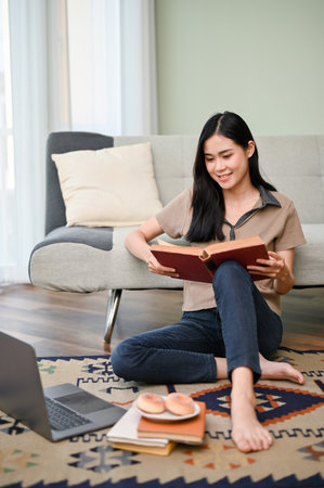 Portrait, Beautiful young Asian female in casual clothes siting on the living room floor, researching information on a book, doing homework.の写真素材